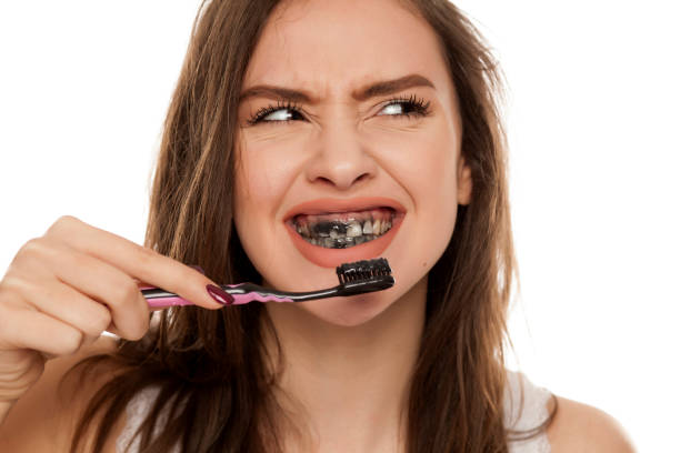 Can I use charcoal toothpaste with braces? Young girl brushing teeth with charcoal toothpaste, black toothpaste in teeth, smiling with confused expression