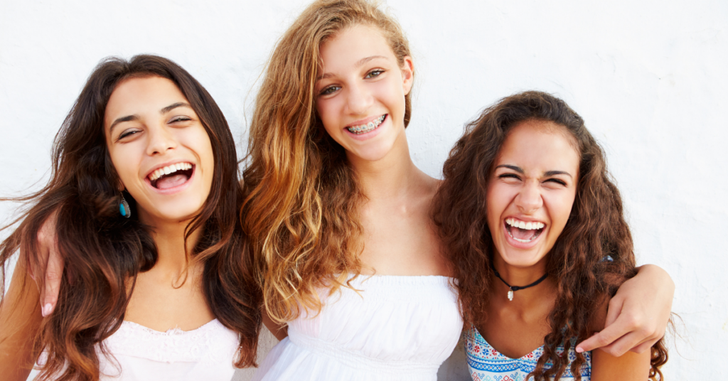 Three girls, best friends standing beside each other smiling, girl in the middle is wearing braces from Cool Braces with Dr. Tahir's orthodontist office