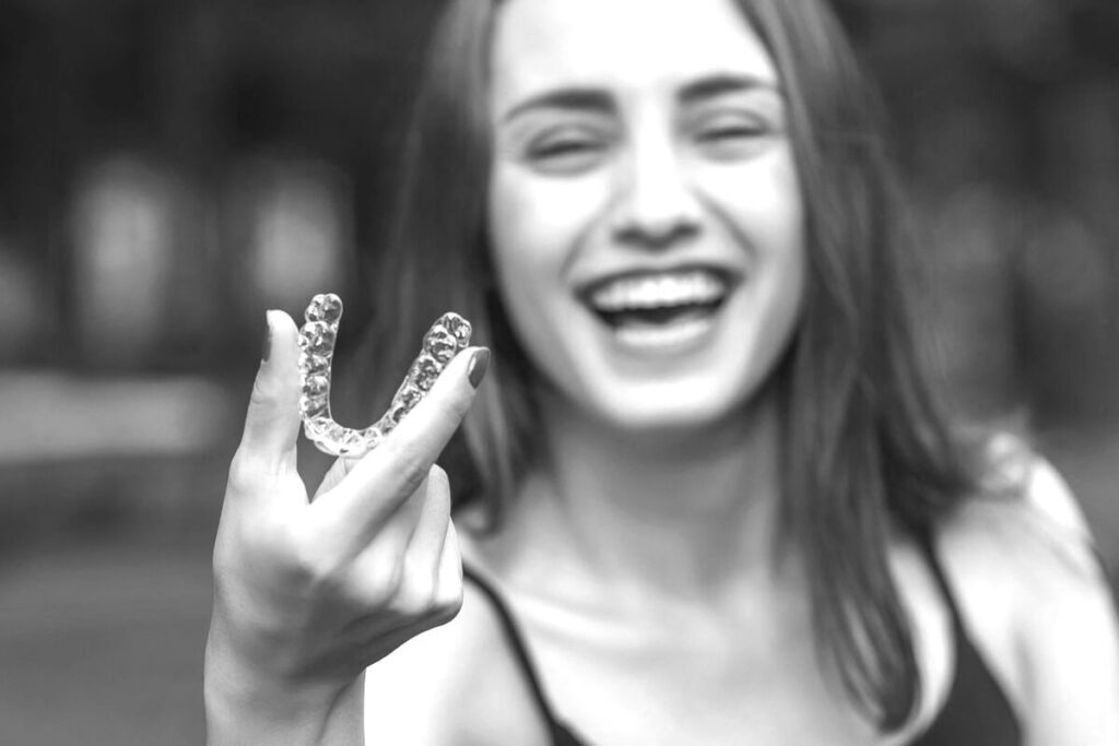 Invisalign, girl holding Invisalign clear aligner, black and white photo, girl smiling wearing tank top at Cool Braces orthodontist office in Berwyn and Oak Lawn